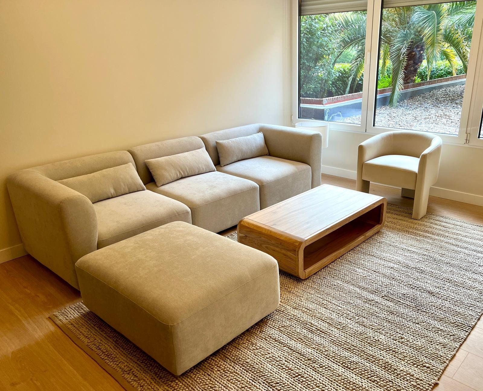 Salón con sofá crema y palmeras tras las ventanas