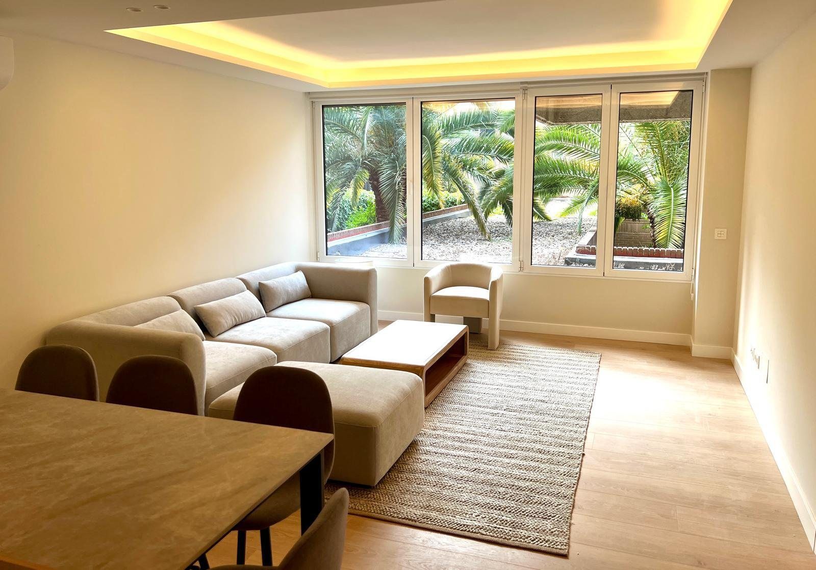 Salón amplio con sofá modular, mesa de comedor y ventanas a la vegetación
